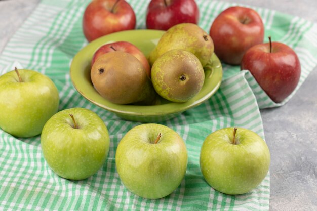 Red and green apples with fresh pear in green bowl.