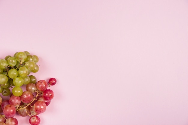 Red and green grapes on the corner of the pink background