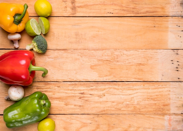 Red; green and yellow bell peppers; mushroom; lemon and broccoli on wooden desk