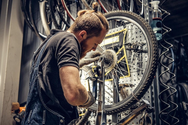 Red hair bearded mechanic removing bicycle rear cassette in a workshop.