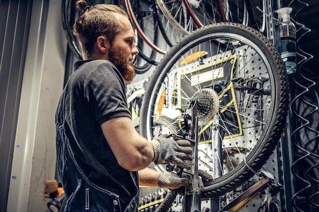 ワークショップで自転車のリアカセットを取り外す赤い髪のひげを生やしたメカニック。