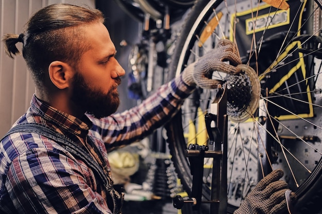 Рыжий бородатый механик снимает заднюю кассету велосипеда в мастерской.