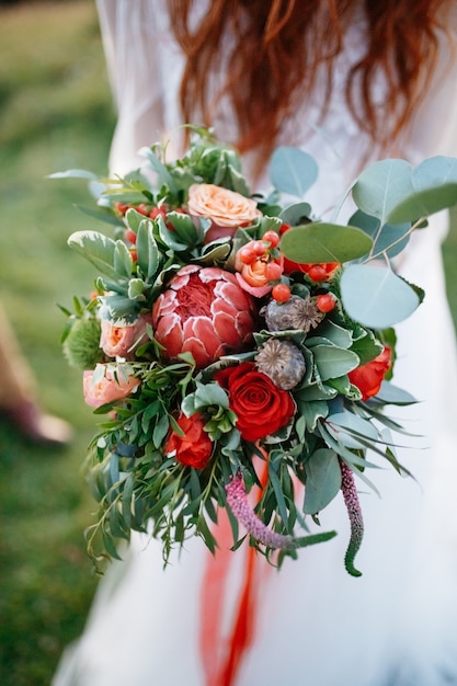 赤い髪の花嫁は赤で作られた完璧な結婚式の花束を保持しています