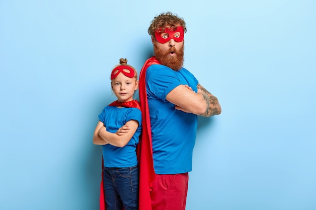 Free photo red haired father and daughter play superhero game together, stand backs, have fun