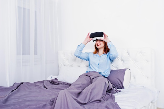 스튜디오 방에서 VR 안경을 쓰고 침대에 누워 있는 빨간 머리 소녀