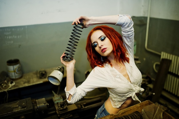 Free photo red haired girl wear on short denim shorts and white blouse with steel spring at hand posed at industrial machine at the factory