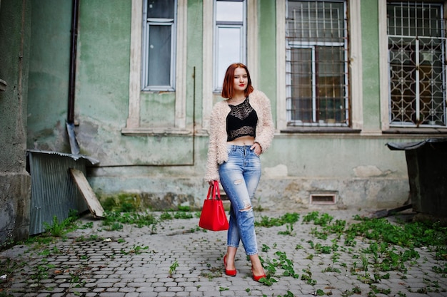 Red haired girl with red handbag posed at street of city
