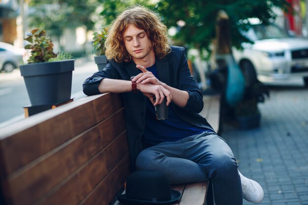 Red haired hipster man sitting on bench looking to his watch