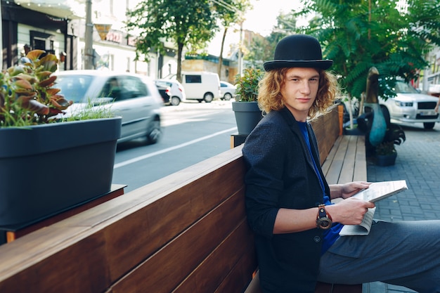 Red haired hipster man sitting on bench with newspaper