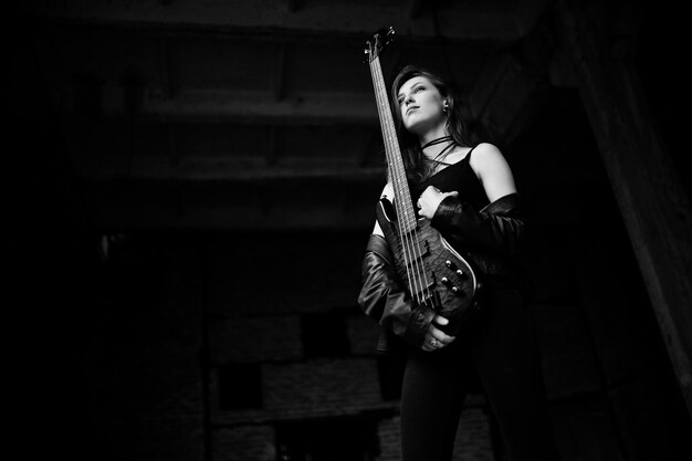 Red haired punk girl wear on black with bass guitar at abadoned place Portrait of gothic woman musician