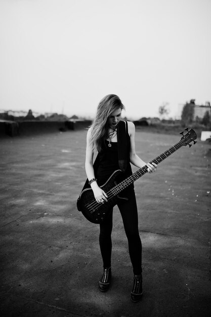 빨간 머리 펑크 소녀는 지붕에서 베이스 기타와 함께 검은색을 입는다