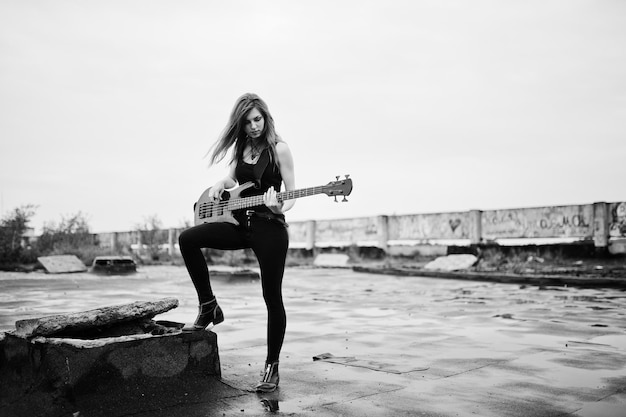 Red haired punk girl wear on black with bass guitar at the roof