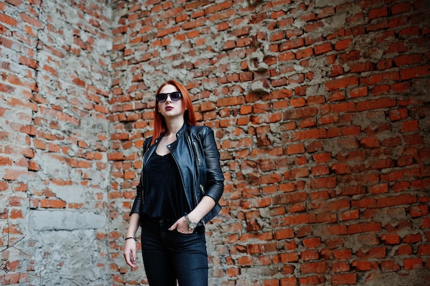 Рыжеволосая стильная девушка в солнцезащитных очках в черном фоне заброшенного места с кирпичными стенами
