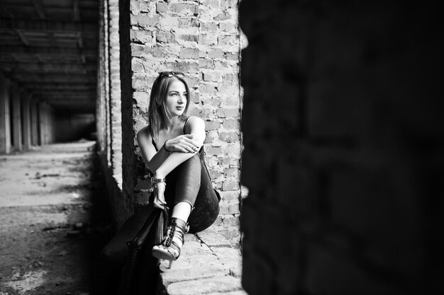 Red haired stylish girl in sunglasses wear in black against abadoned place with brick walls