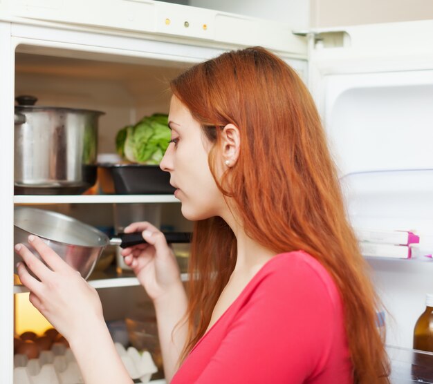 Рыжеволосая женщина ищет что-то в холодильнике