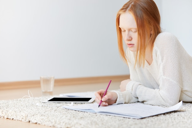 Red-haired woman lying on floor with notebook and tablet