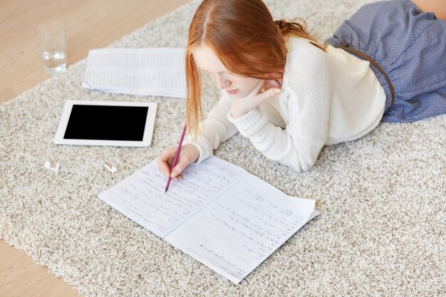 Red-haired woman lying on floor with notebook and tablet