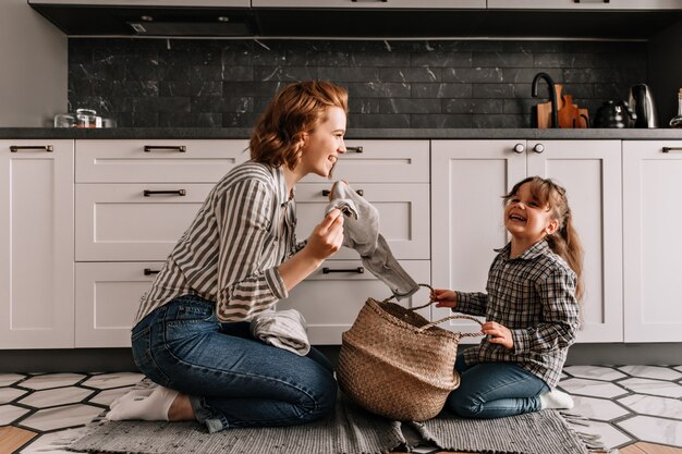 Red-haired woman tells jokes to her daughter and takes out dirty clothes from basket.