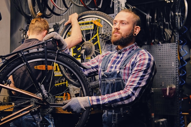 Red head bearded mechanic fixing rear derailleur from a bicycle in a workshop.