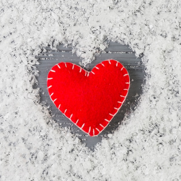 Cuore rosso tra neve decorativa sullo scrittorio di legno