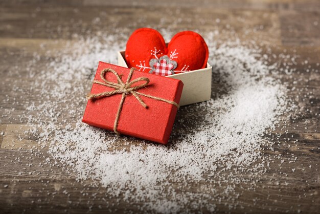 Red heart in gift box on wooden board with snow