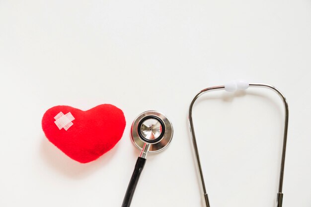 Red heart with bandages and stethoscope on white background