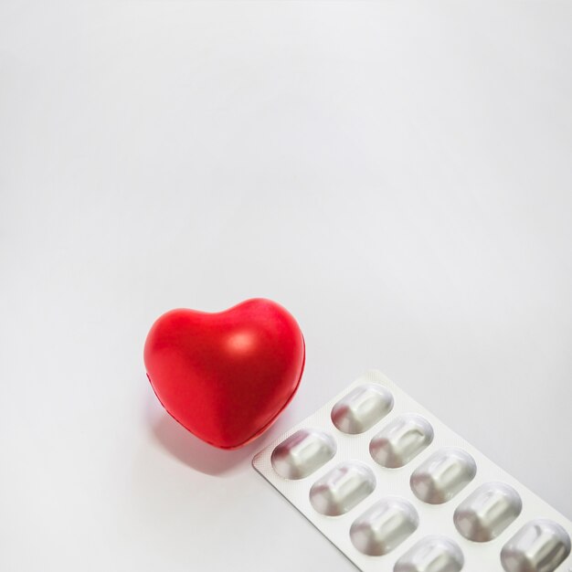 Красное сердце с серебряными упакованными таблетками на белом фоне
