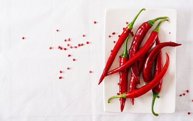 Red hot chili peppers in plate on white table. Top view. Flat lay