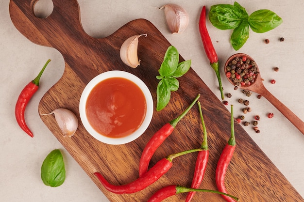 Free photo red hot chilli sauce. tomato ketchup, chilli sauce, puree with chili pepper, tomatoes and garlic. on wooden cutting board on stone surface. top view.