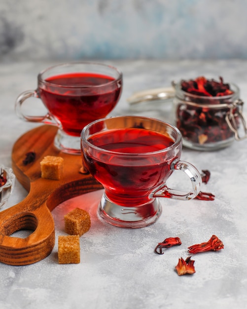 Red Hot Hibiscus tea in a glass mug on concrete  with dry hibiscus petals 