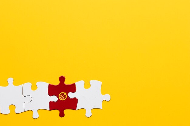 Red jigsaw puzzle piece with dartboard symbol arranged with white piece on yellow background