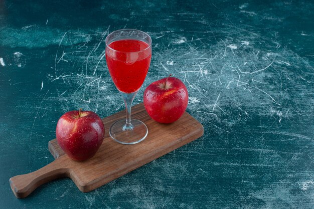 red juice and apple on the board , on the blue table. 