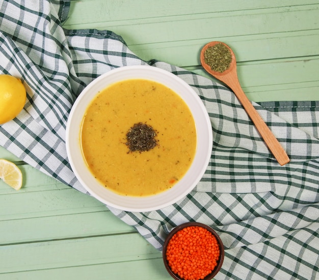 Red lentil soup with herbs in the white bowl on the checked tablecloth.