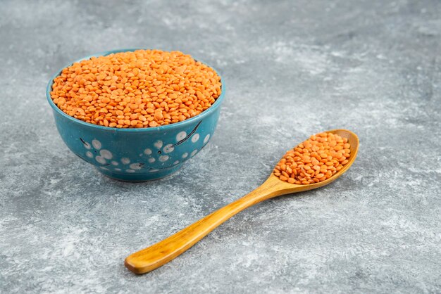 Red lentils in blue bowl with wooden spoon on marble surface.