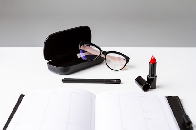 Free photo red lipstick glasses and notebook over white surface