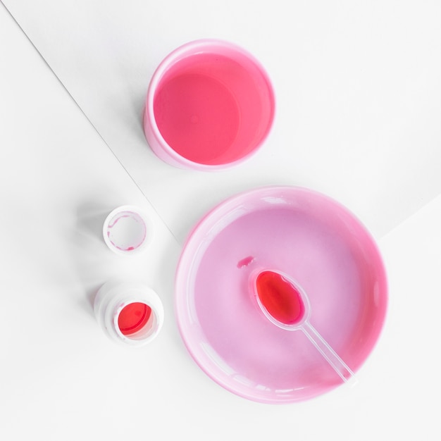 Red liquid medicine in spoon on the pink plate with bottle and glass on white paper