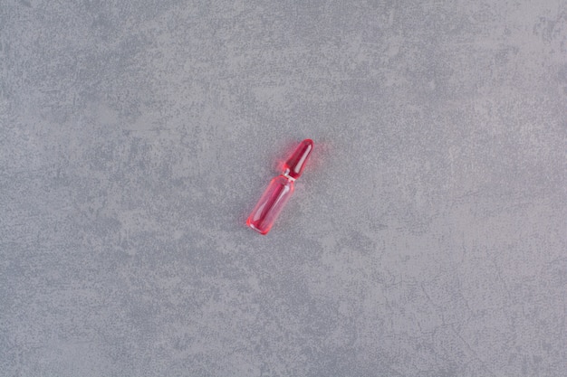 Red medical ampoule on marble table.