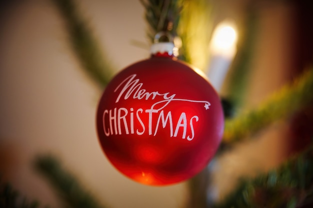 Free photo red merry christmas bauble hanging from christmas tree