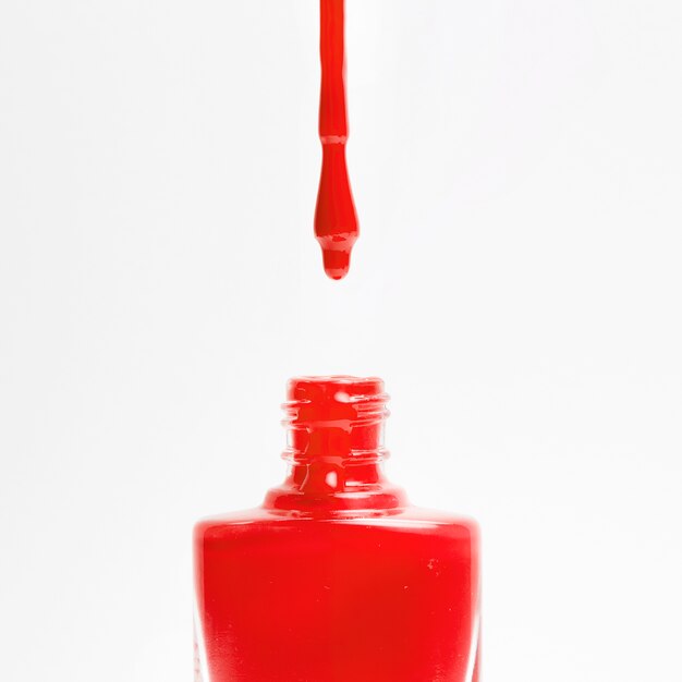 Red nail polish dripping from the brush in bottle on white background