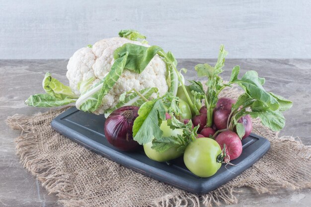 Red onion, cauliflower, green tomato, turnips and turnip leaves on a black platter on marble surface