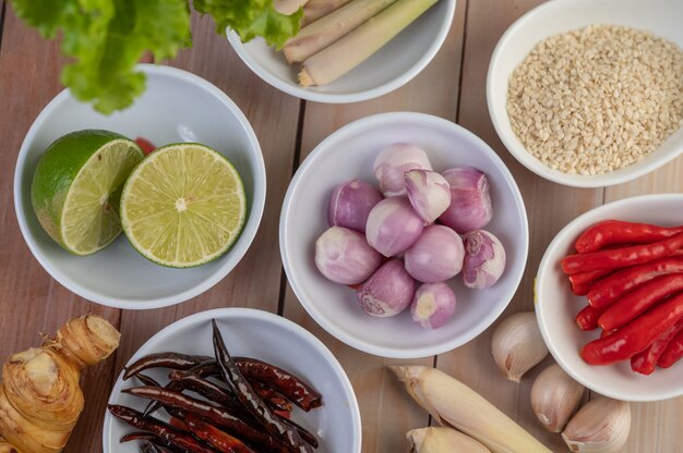 Red onions, lemon, lemongrass, chilies, garlic, galangal, and lettuce in a cup on a wooden floor.