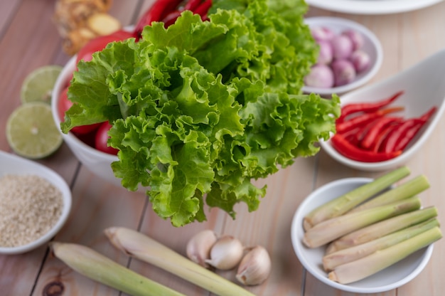 Cipolle rosse, limone, citronella, peperoncino, aglio, galanga e lattuga in una tazza su un pavimento di legno.