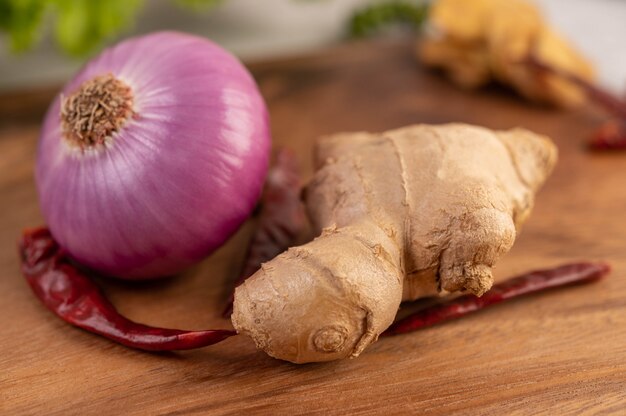 Red onions, peppers, and ginger on a wooden table.