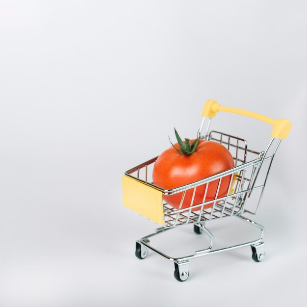 Red organic tomato in shopping cart on white background