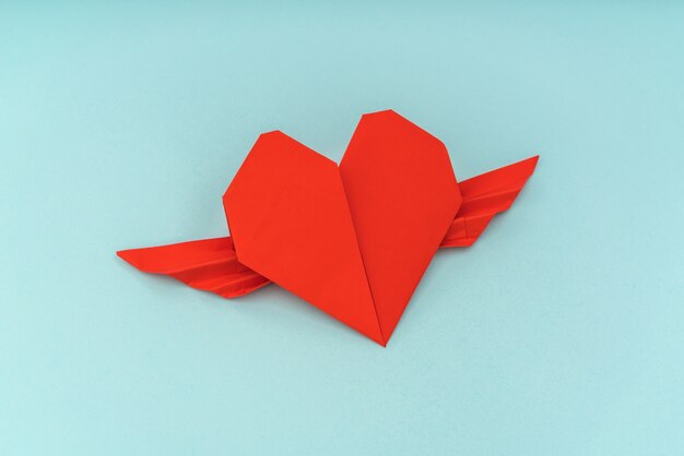 青い背景上の翼を持つ赤い紙折り紙の心。