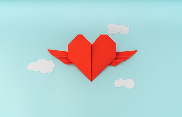 Red paper origami heart with wings and cloud on blue background