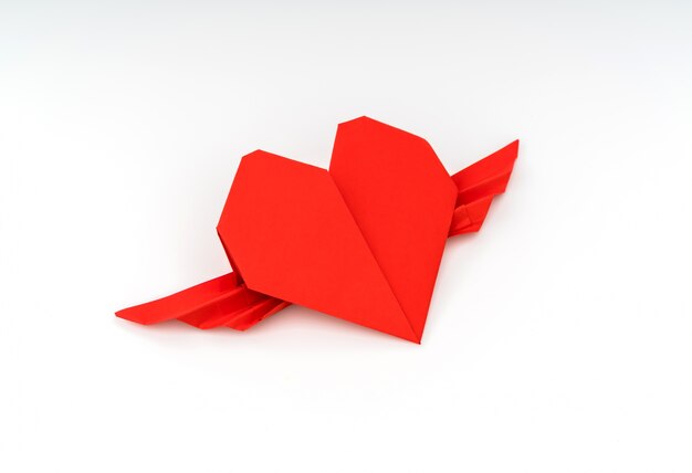 白い背景の上の翼を持つ赤い紙折り紙の心。
