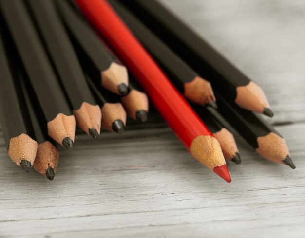 Red pencil stands out from the crowd of black pencil on a wooden white background.