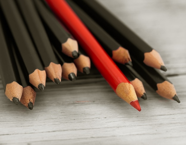 赤鉛筆は木製の白い背景に黒の鉛筆の群衆から目立ちます。