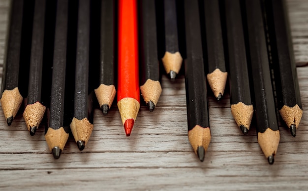 Free photo red pencil stands out from the crowd of black pencil on a wooden white background.